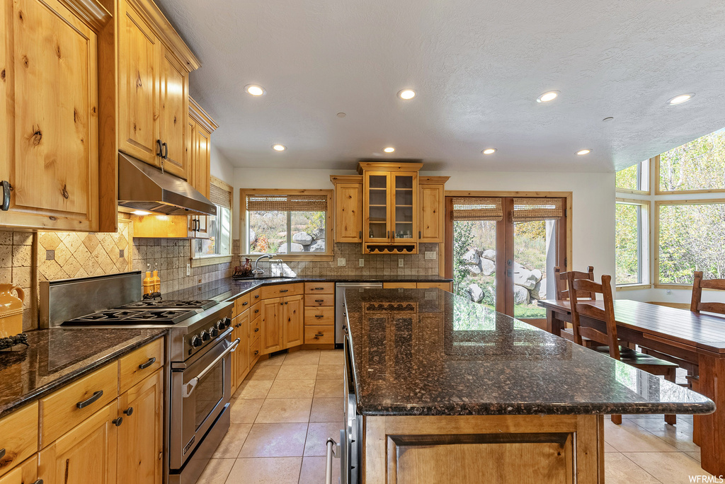 Kitchen featuring light tile floors, dark stone counters, a kitchen island, tasteful backsplash, and stainless steel appliances