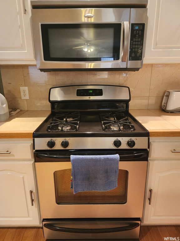 Kitchen featuring backsplash, light hardwood floors, stainless steel appliances, and white cabinets