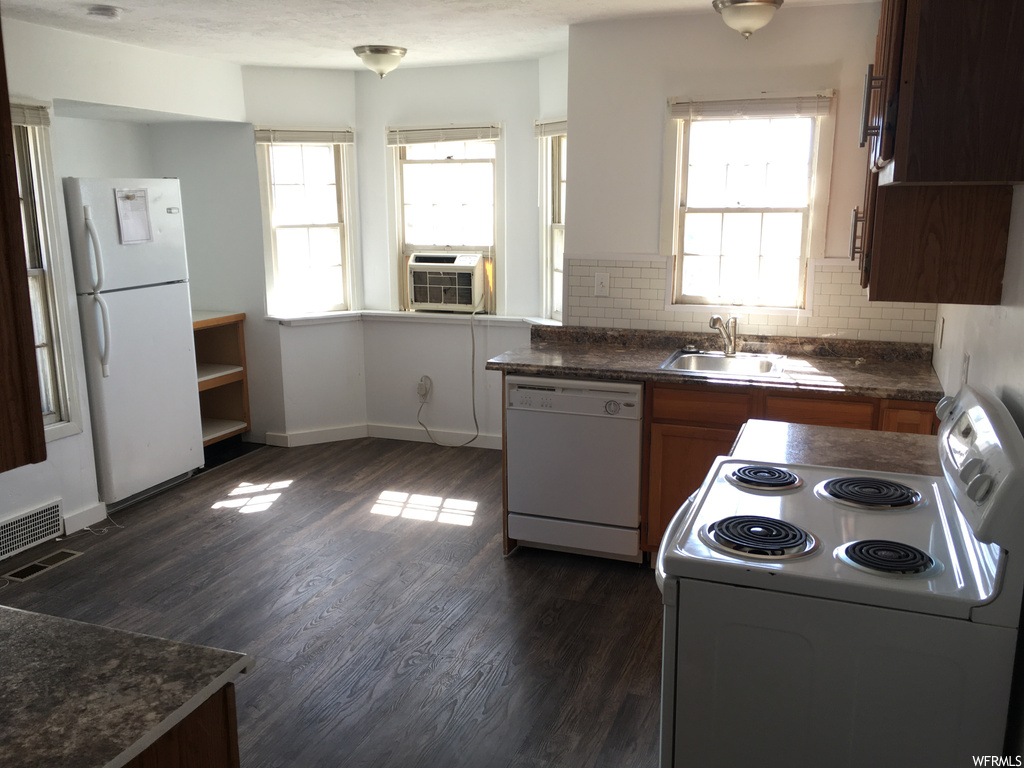Kitchen featuring tasteful backsplash, a healthy amount of sunlight, dark hardwood floors, white appliances, and sink