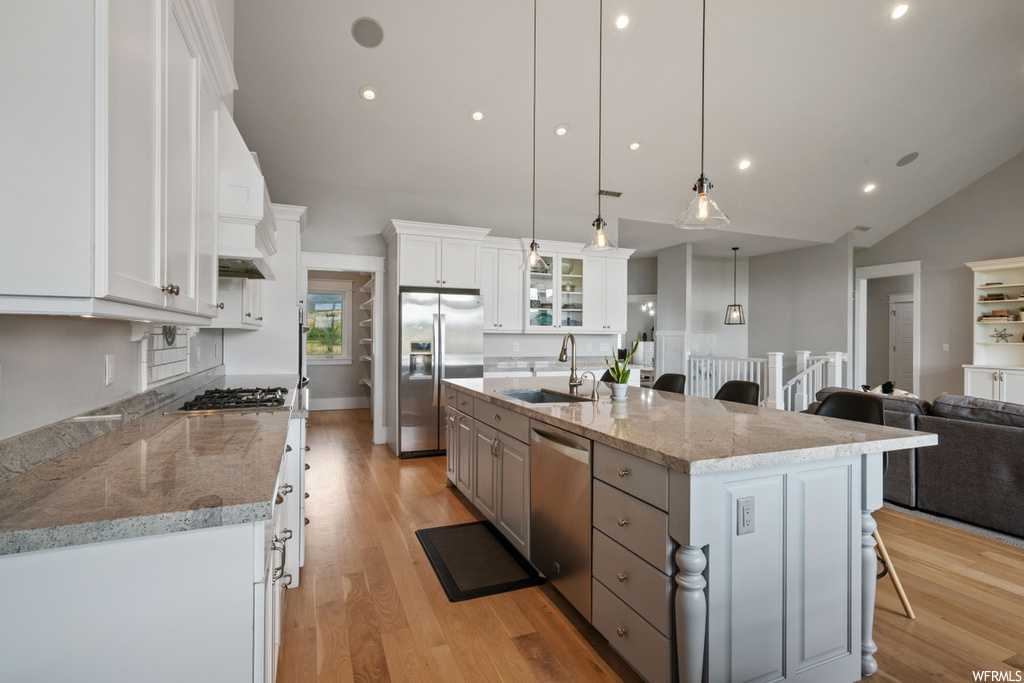 Kitchen featuring decorative light fixtures, sink, a kitchen island with sink, light hardwood flooring, and white cabinetry