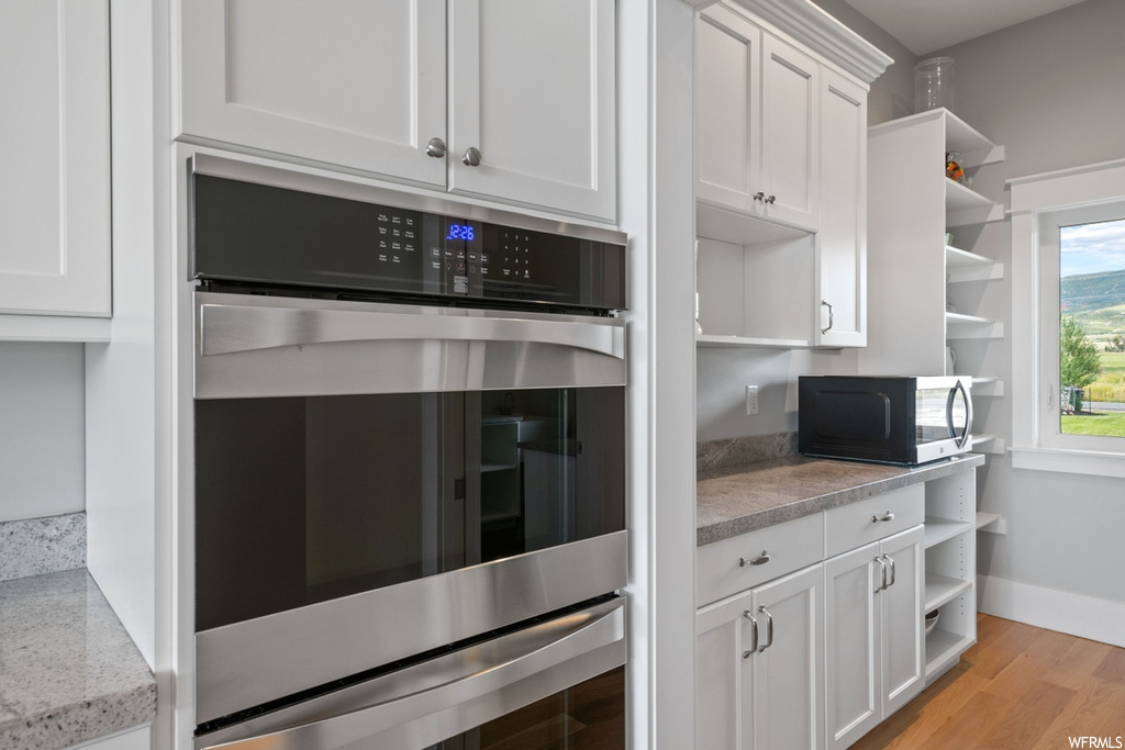 Kitchen featuring white cabinetry, light stone countertops, light hardwood floors, and stainless steel double oven