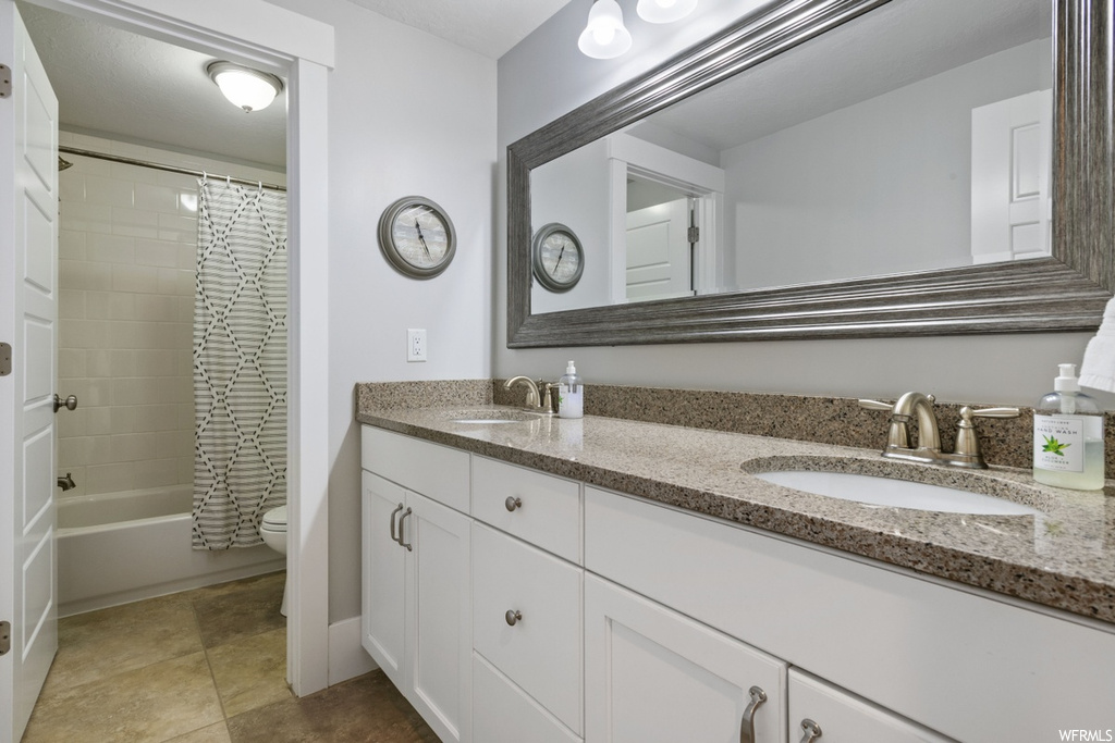 Full bathroom with tile floors, toilet, shower / tub combo with curtain, and dual vanity