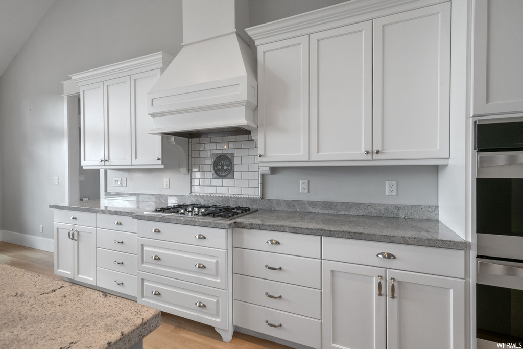 Kitchen featuring backsplash, light hardwood floors, white cabinets, and custom exhaust hood