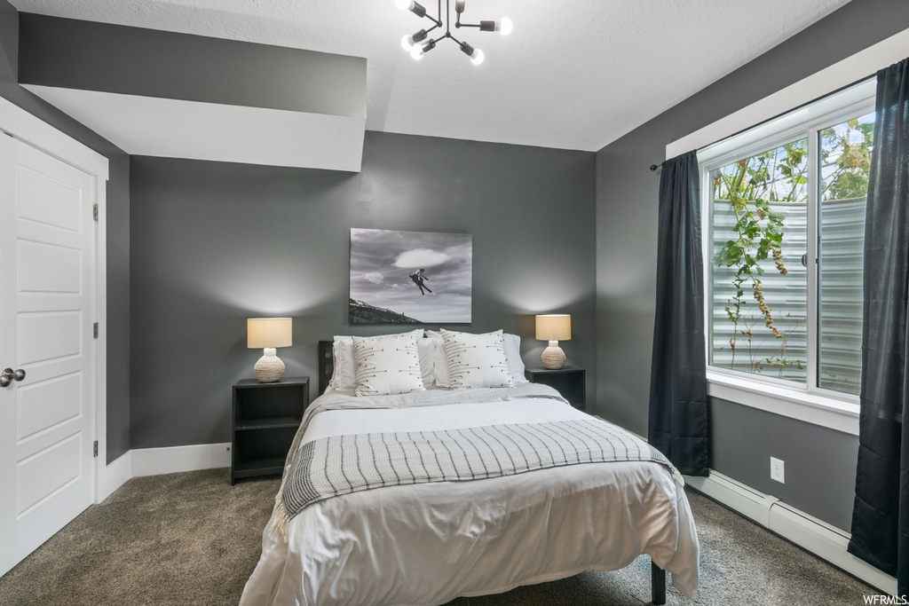 Bedroom with a baseboard heating unit, an inviting chandelier, and dark colored carpet