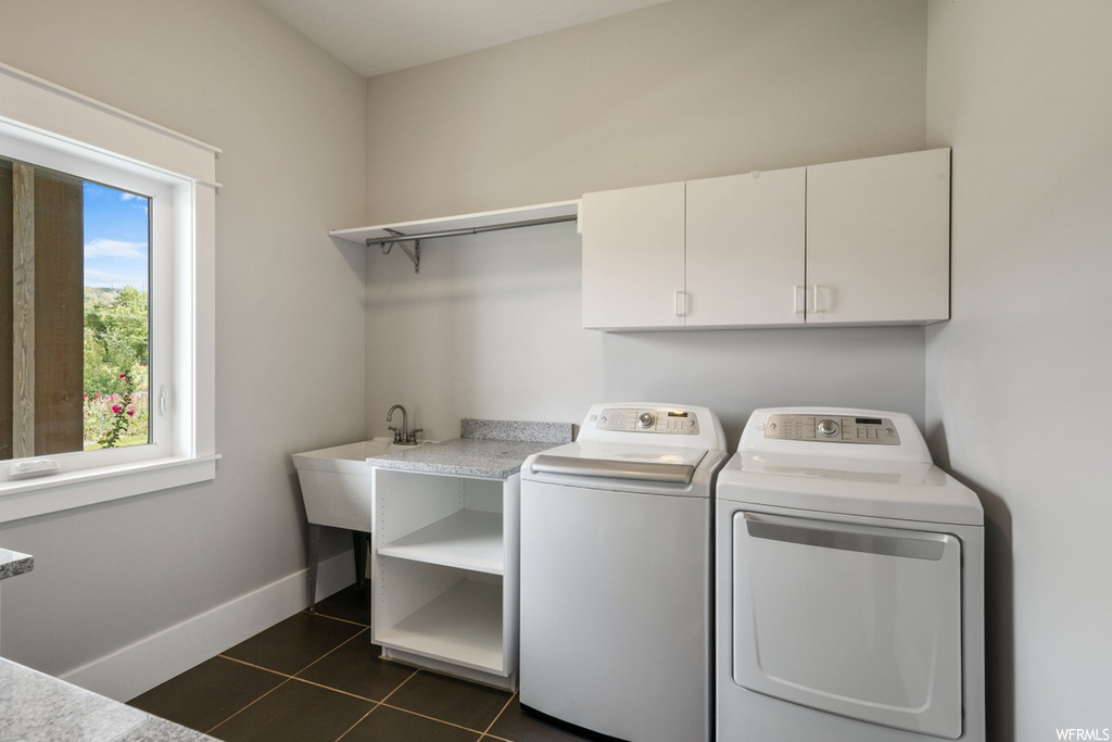 Clothes washing area featuring sink, washer and dryer, cabinets, and dark tile floors