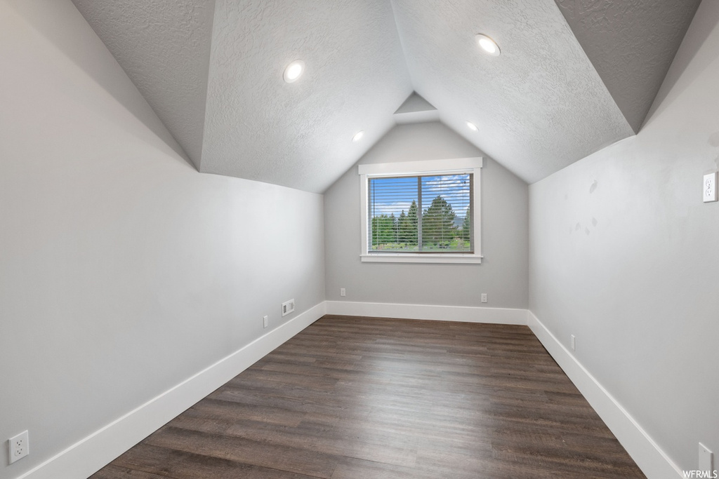 Bonus room with lofted ceiling, dark hardwood flooring, and a textured ceiling