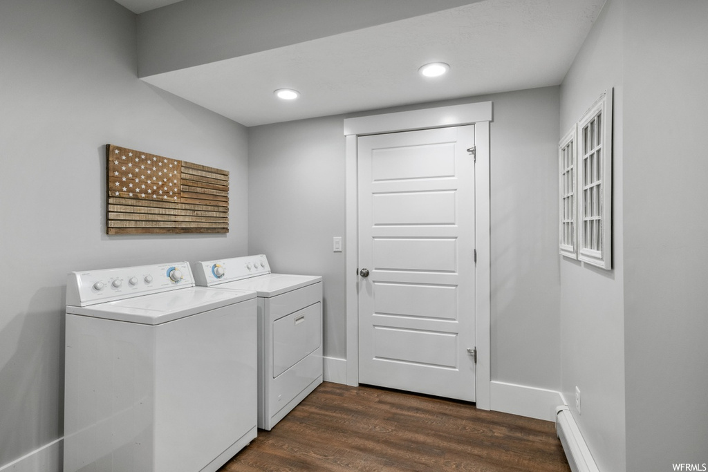 Clothes washing area with dark hardwood flooring, washer and dryer, and baseboard heating