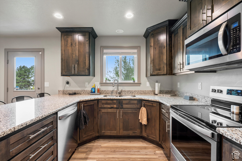 Kitchen featuring sink, light hardwood / wood-style floors, stainless steel appliances, and light stone countertops