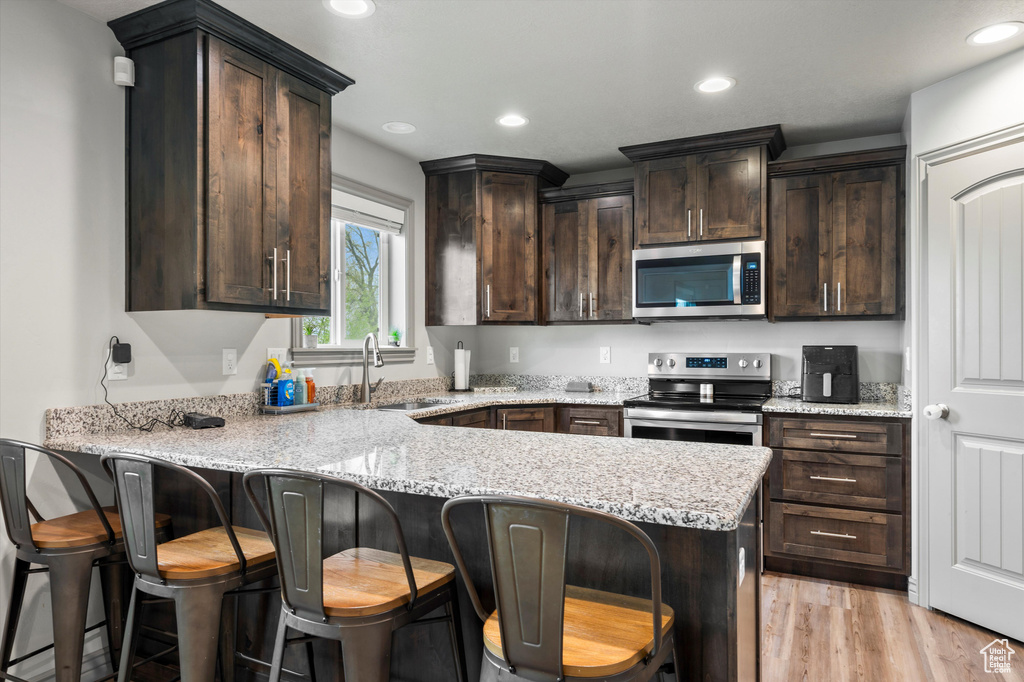 Kitchen featuring light stone countertops, stainless steel appliances, sink, light hardwood / wood-style floors, and dark brown cabinetry