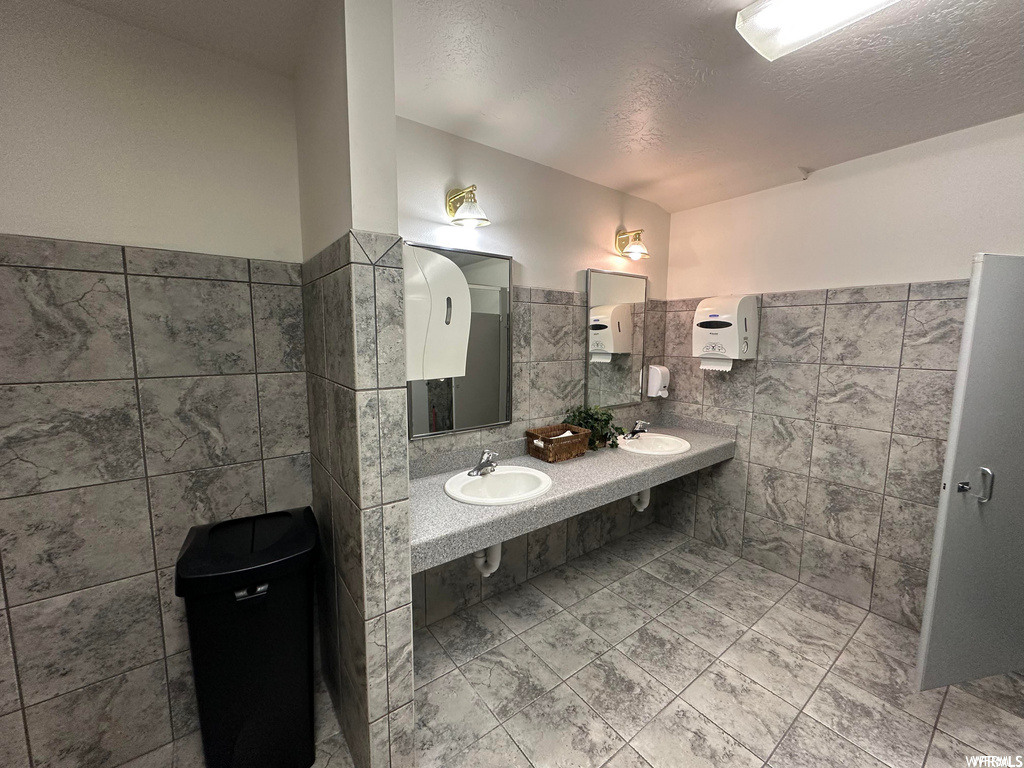 Bathroom featuring a textured ceiling, double sink vanity, tile walls, and tile flooring