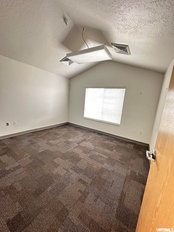 Spare room with a textured ceiling, vaulted ceiling, and carpet