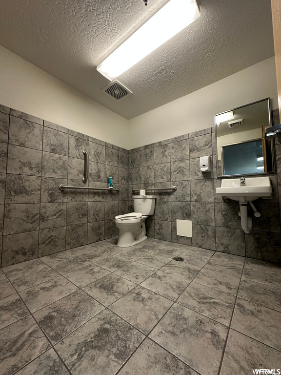 Bathroom featuring sink, toilet, a textured ceiling, tile walls, and tile floors