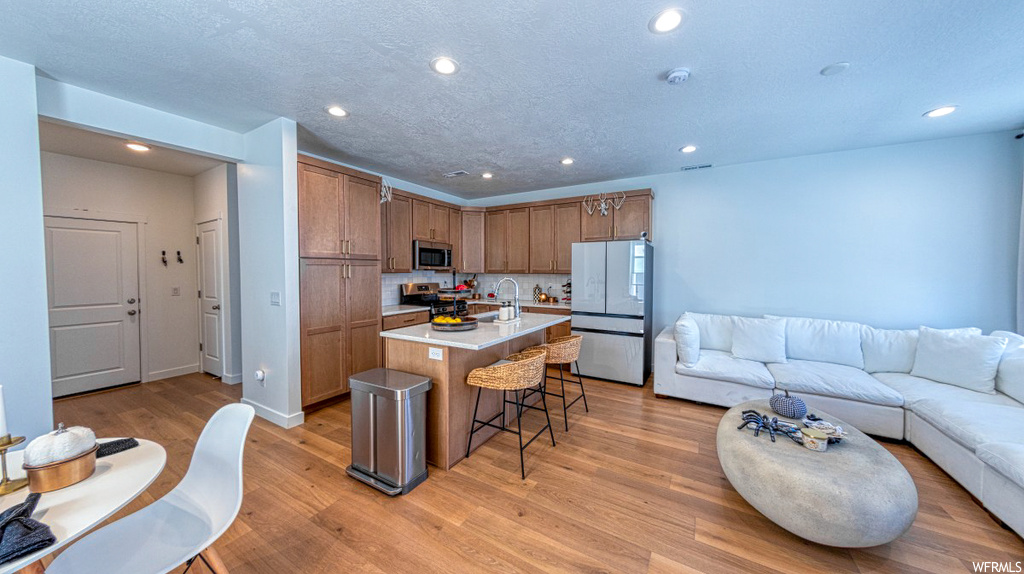 Kitchen featuring a center island with sink, a breakfast bar, stainless steel appliances, and light hardwood floors