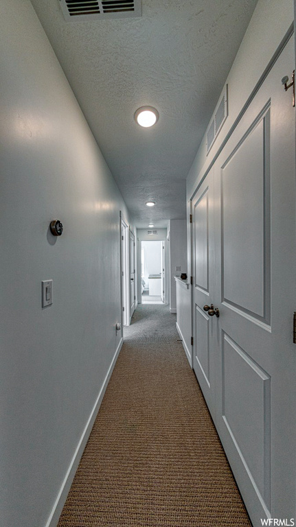 Corridor featuring light colored carpet and a textured ceiling