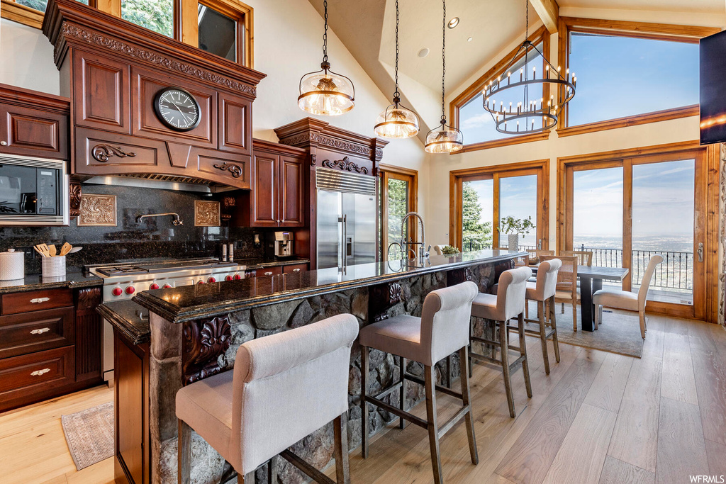 Kitchen featuring high vaulted ceiling, a chandelier, tasteful backsplash, built in appliances, and light hardwood / wood-style flooring
