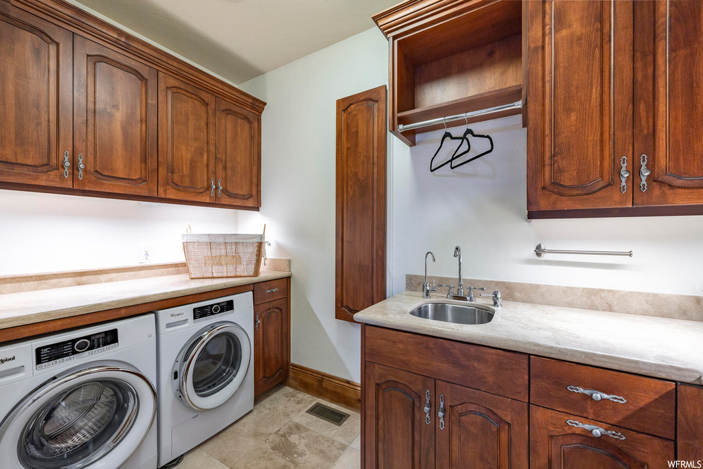 Washroom featuring cabinets, sink, washing machine and dryer, and light tile floors