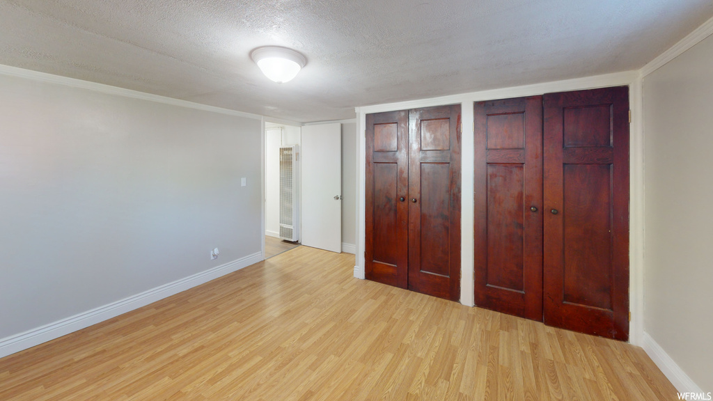 Unfurnished bedroom with a textured ceiling, crown molding, light hardwood flooring, and two closets