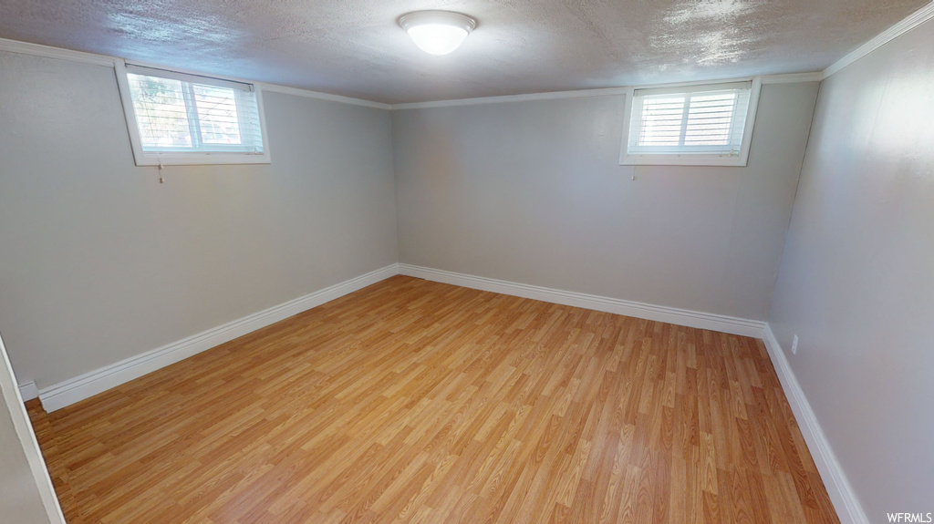 Basement with crown molding, light hardwood floors, and a textured ceiling