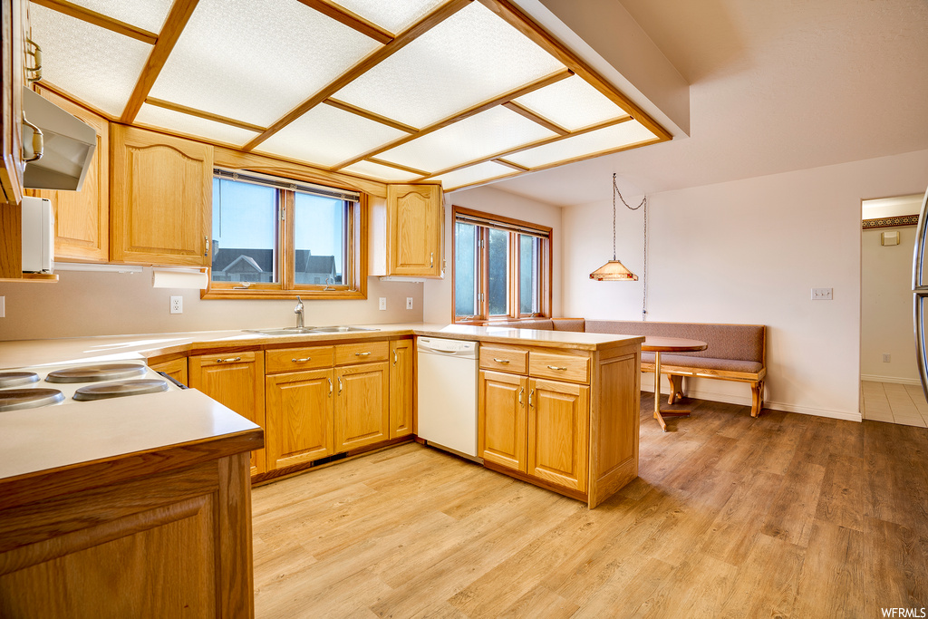 Kitchen with sink, wall chimney range hood, light hardwood flooring, pendant lighting, and kitchen peninsula