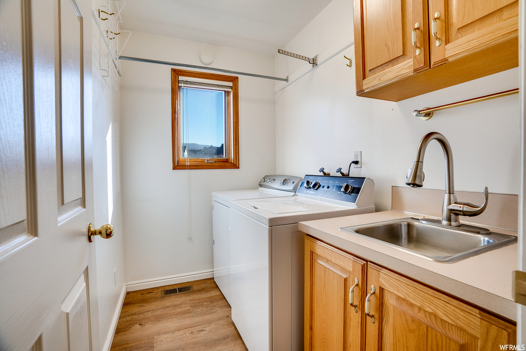Laundry area featuring sink, cabinets, light hardwood floors, and washing machine and dryer