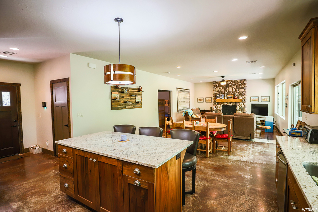 Kitchen featuring a fireplace, a kitchen island, hanging light fixtures, a kitchen bar, and light stone counters