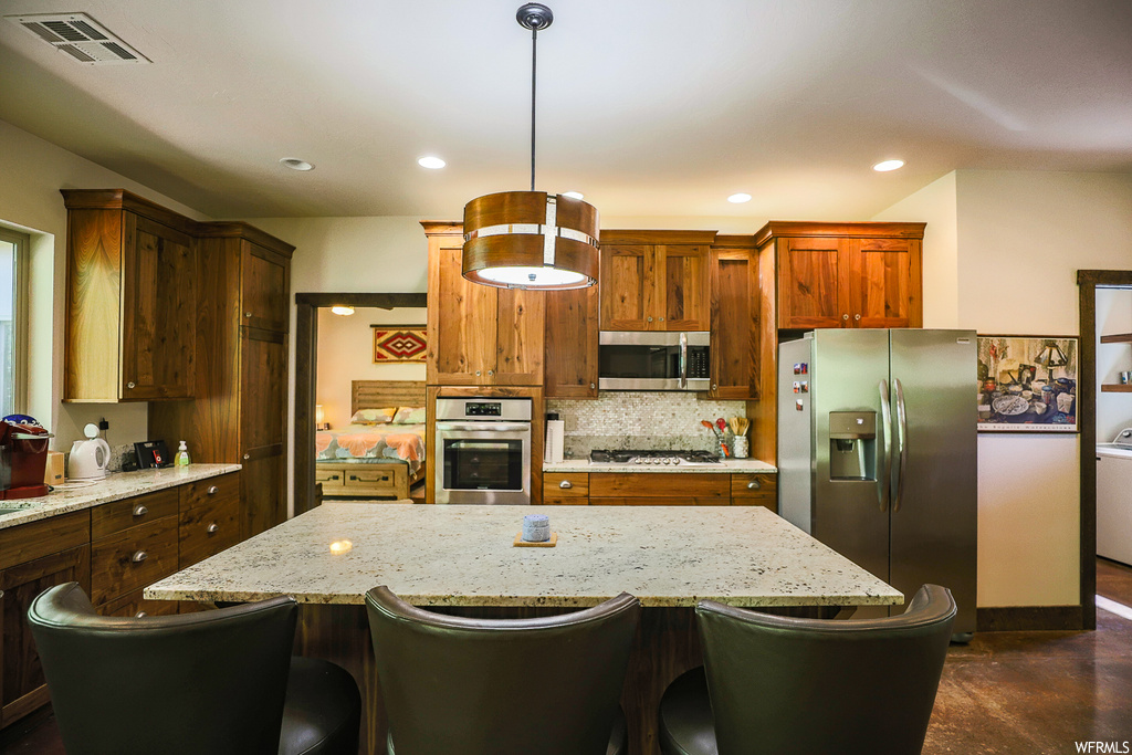 Kitchen with backsplash, a center island, appliances with stainless steel finishes, a kitchen bar, and decorative light fixtures