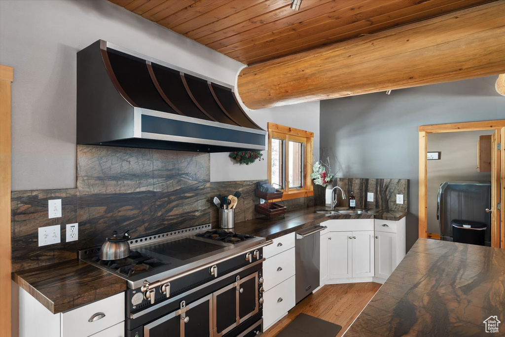 Kitchen featuring custom range hood, stainless steel dishwasher, wooden ceiling, a sink, and range