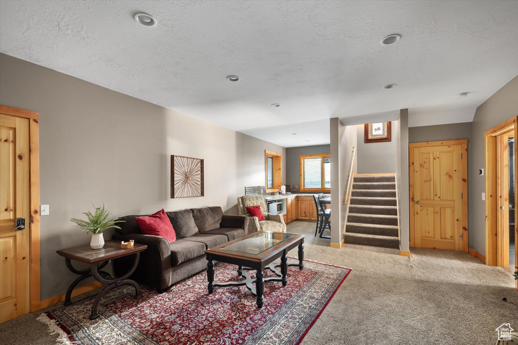 Living area with stairway, light carpet, a textured ceiling, and baseboards