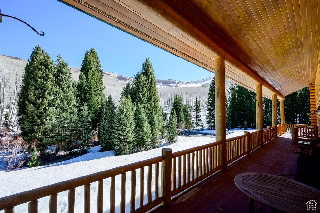 Snow covered deck featuring a mountain view, covered porch, and a forest view