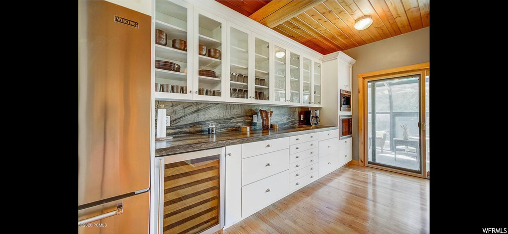 Kitchen featuring beverage cooler, backsplash, wooden ceiling, light hardwood flooring, and white cabinetry