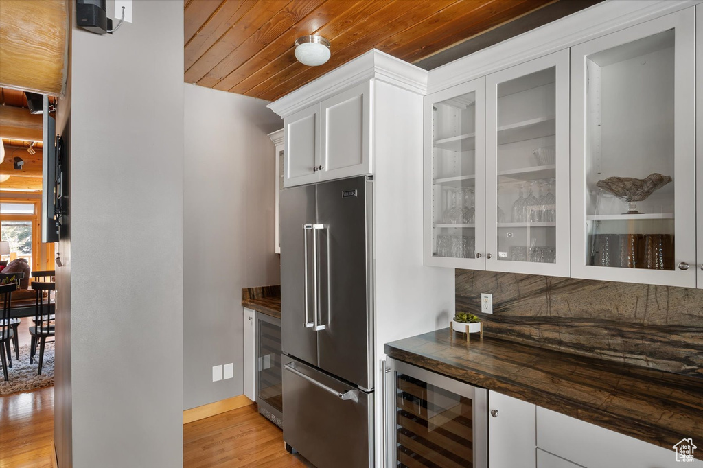 Kitchen with high quality fridge, wine cooler, light wood-style flooring, wood ceiling, and glass insert cabinets