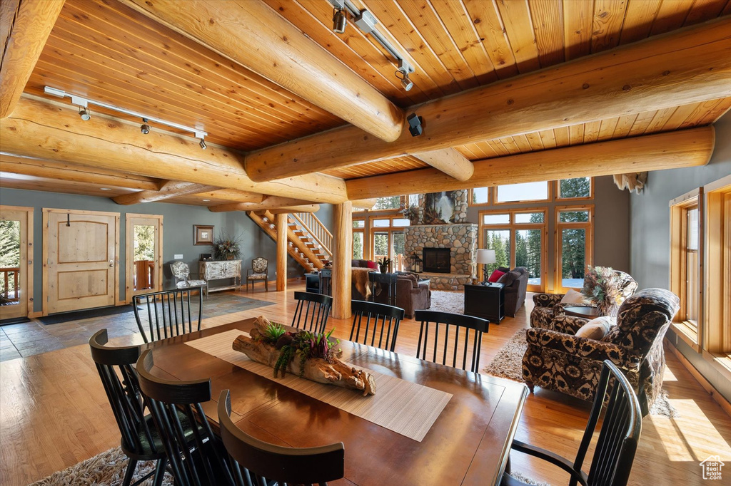 Dining space featuring wood ceiling, wood-type flooring, a stone fireplace, track lighting, and beam ceiling