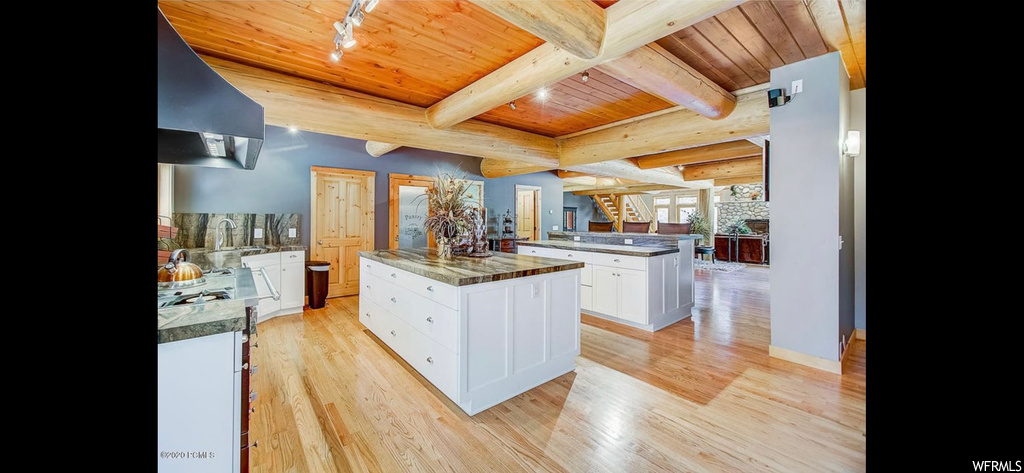 Kitchen featuring white cabinets, wooden ceiling, light hardwood flooring, a kitchen island, and wall chimney exhaust hood