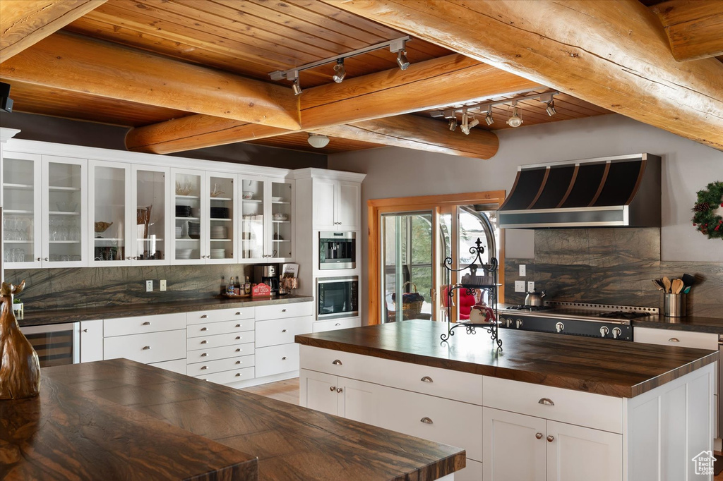 Kitchen featuring butcher block counters, wall chimney range hood, beverage cooler, decorative backsplash, and wooden ceiling