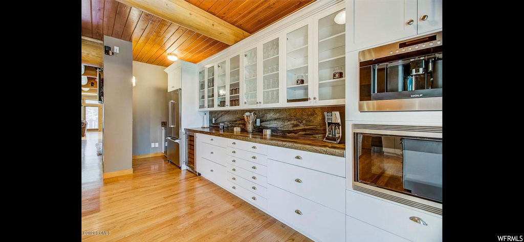 Kitchen with wood ceiling, white cabinets, light hardwood floors, beamed ceiling, and tasteful backsplash