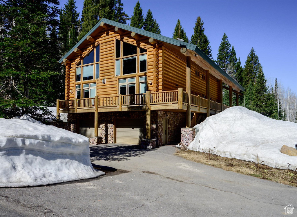 View of property exterior with log exterior, stone siding, a garage, and driveway