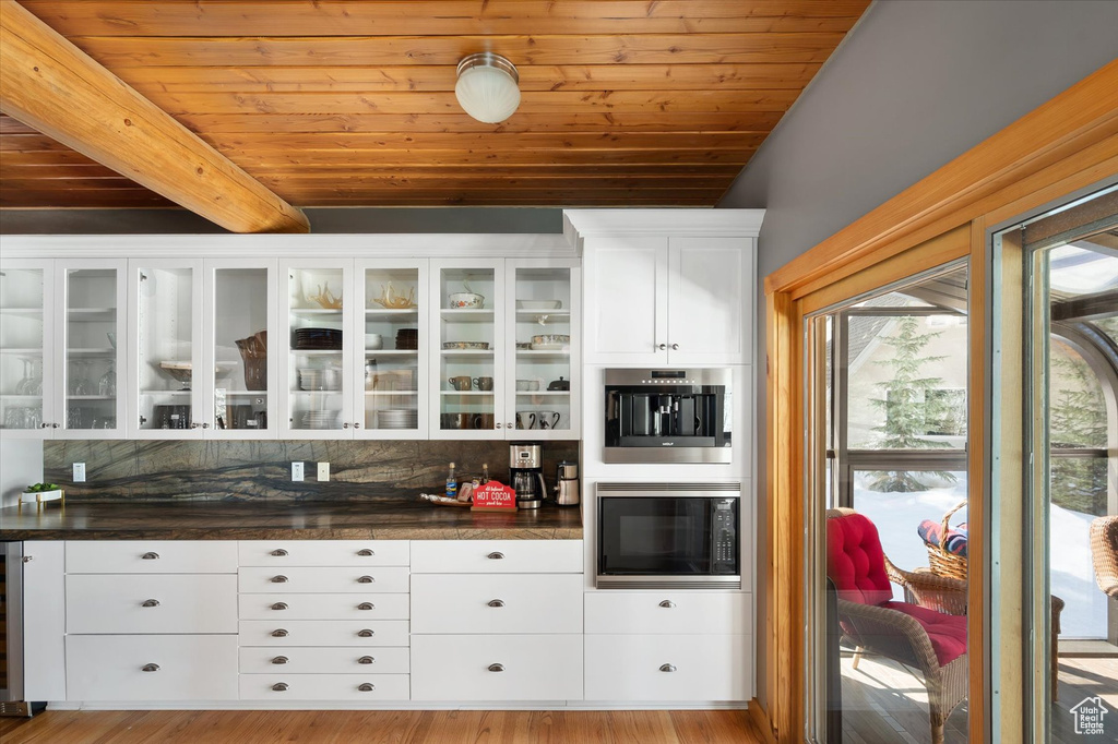 Bar area featuring black microwave, wood ceiling, tasteful backsplash, beam ceiling, and wood finished floors