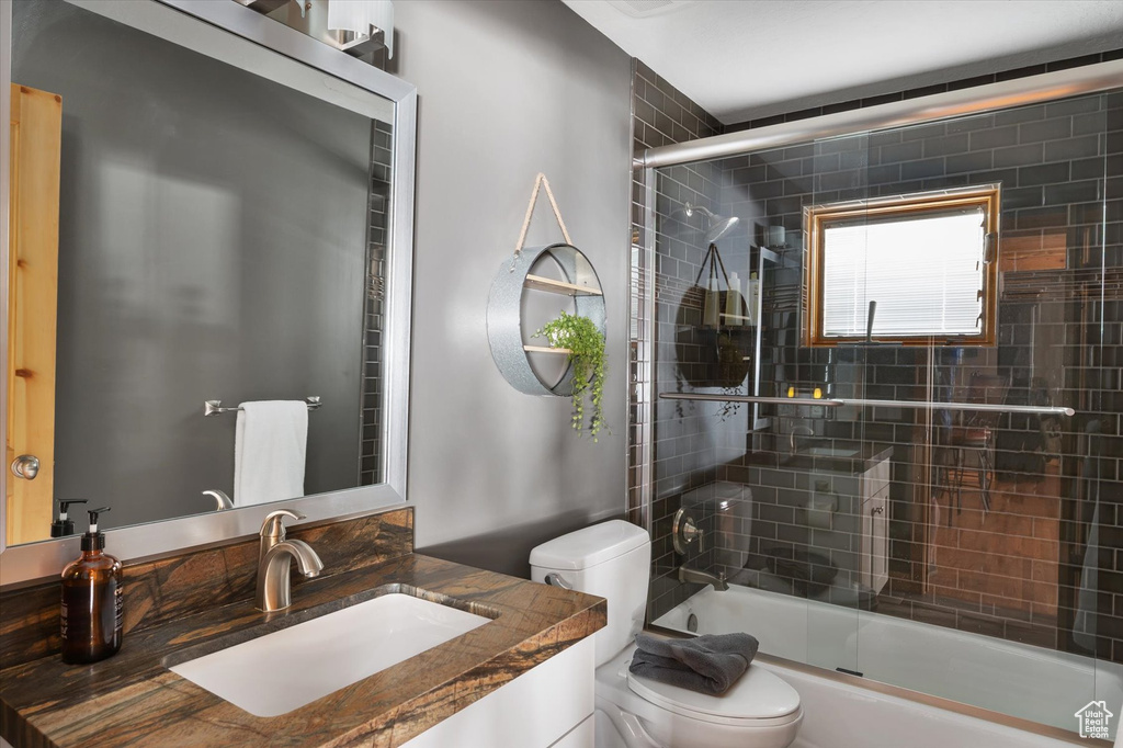 Full bathroom featuring toilet, shower / bath combination with glass door, and vanity
