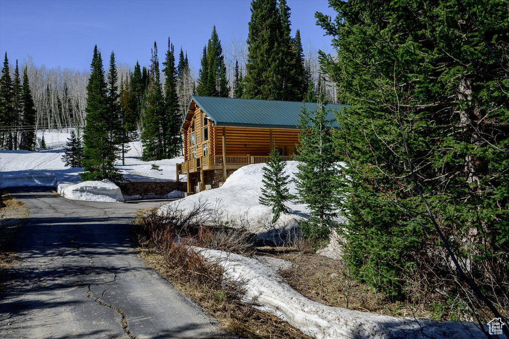 View of snow covered exterior featuring log exterior, metal roof, and a view of trees