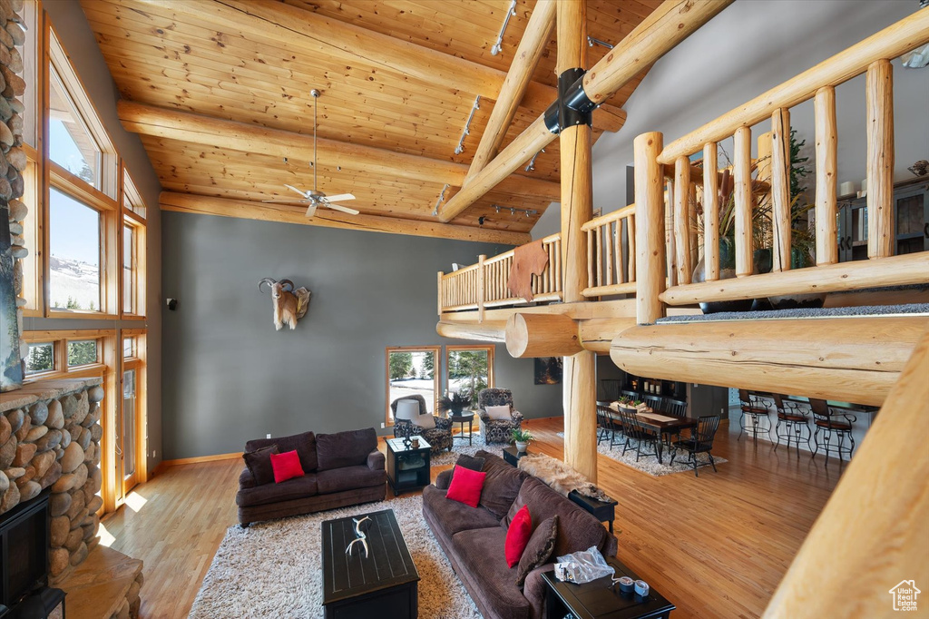 Living area featuring wooden ceiling, a ceiling fan, wood finished floors, a stone fireplace, and high vaulted ceiling