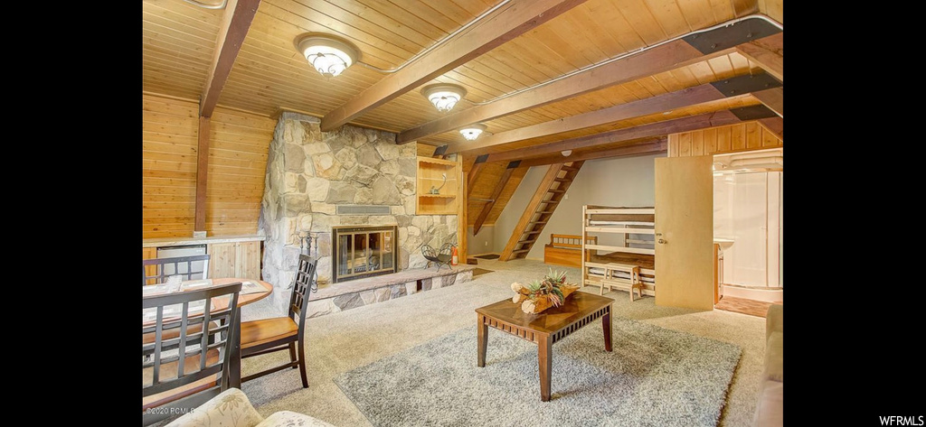 Carpeted living room featuring wood ceiling, a fireplace, wooden walls, and beamed ceiling