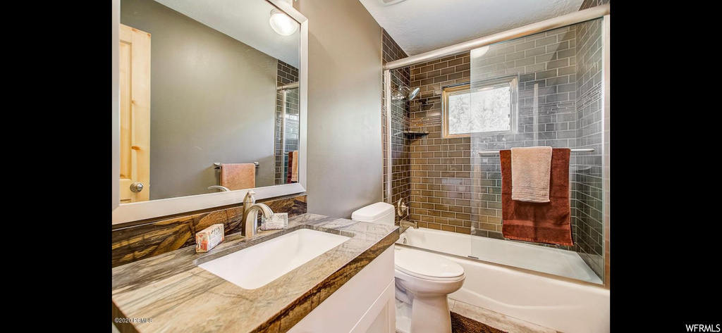 Full bathroom with toilet, vanity, and enclosed tub / shower combo