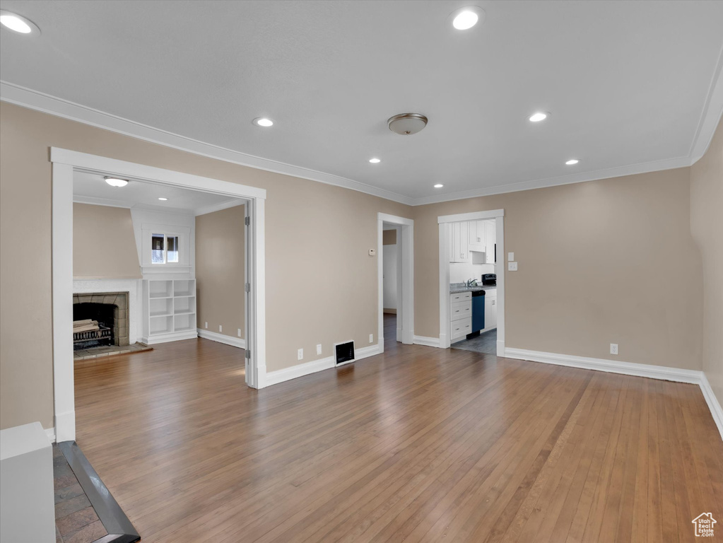 Unfurnished living room with hardwood / wood-style flooring, crown molding, and a tiled fireplace