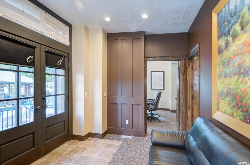 Foyer entrance with a textured ceiling, light colored carpet, and french doors