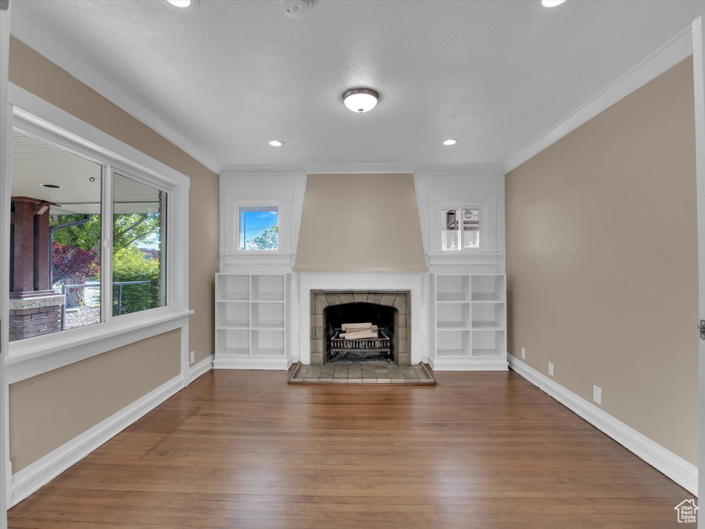 Unfurnished living room with hardwood / wood-style floors, crown molding, a tile fireplace, and built in shelves