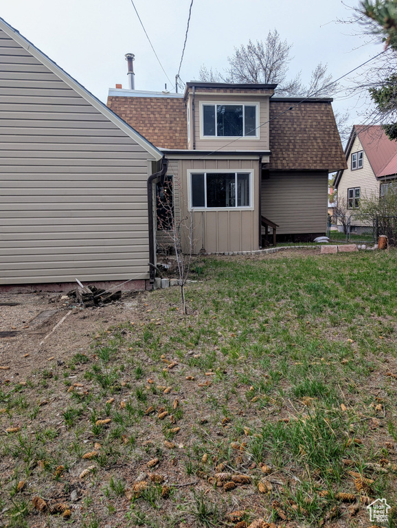 Rear view of house featuring a chimney, board and batten siding, a shingled roof, and a lawn