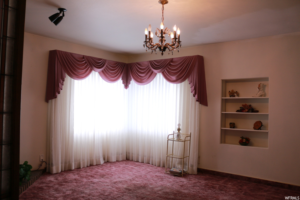Spare room featuring a notable chandelier, built in features, and carpet