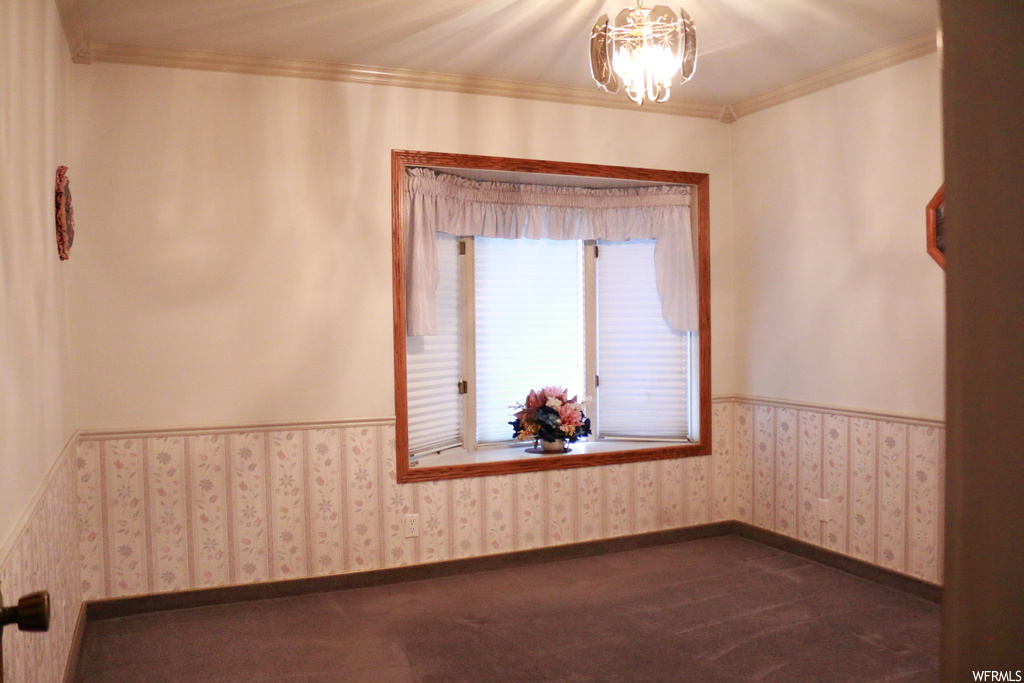 Unfurnished room featuring crown molding, dark colored carpet, and a chandelier