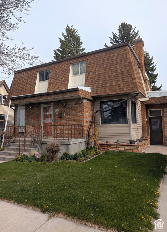 View of front of house with a front lawn, covered porch, a chimney, roof with shingles, and mansard roof