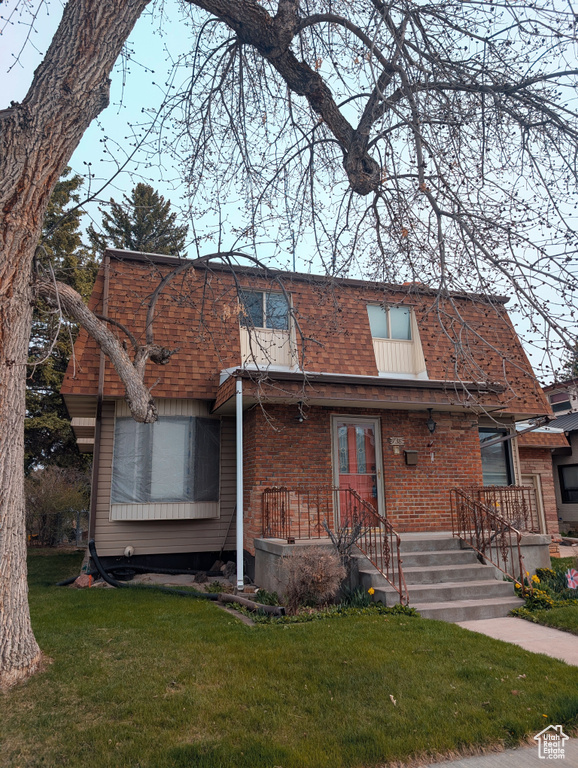 View of front of home with brick siding, a front yard, mansard roof, and roof with shingles
